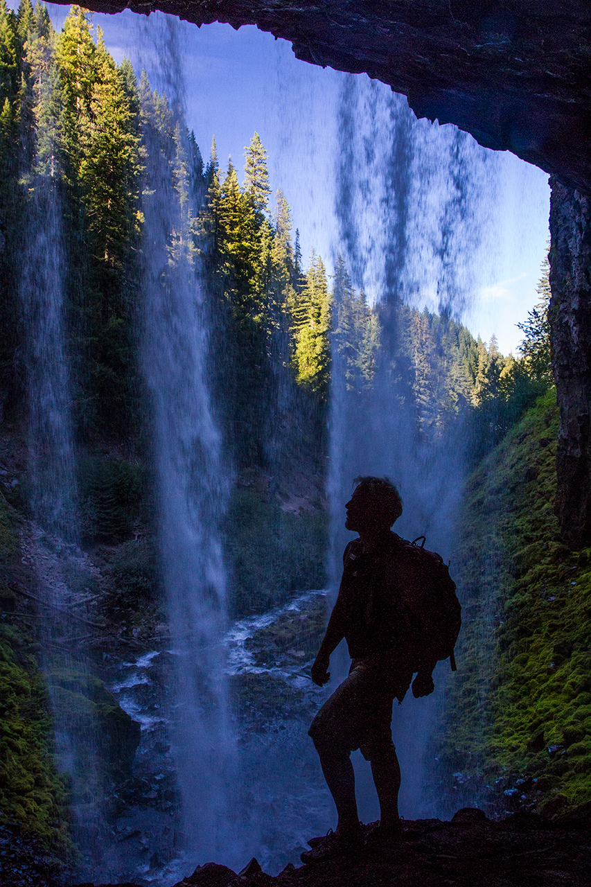 Silhouette of hiker behind the curtain of wilderness waterfall